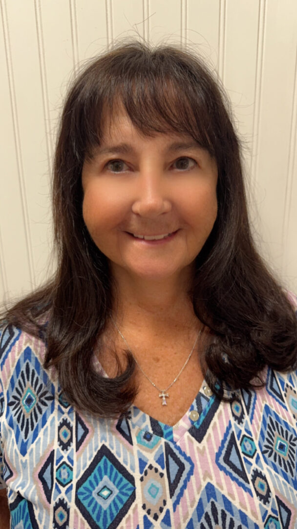 Smiling woman with long brown hair in patterned top and cross necklace. Smiling woman with long brown hair in patterned top and cross necklace.